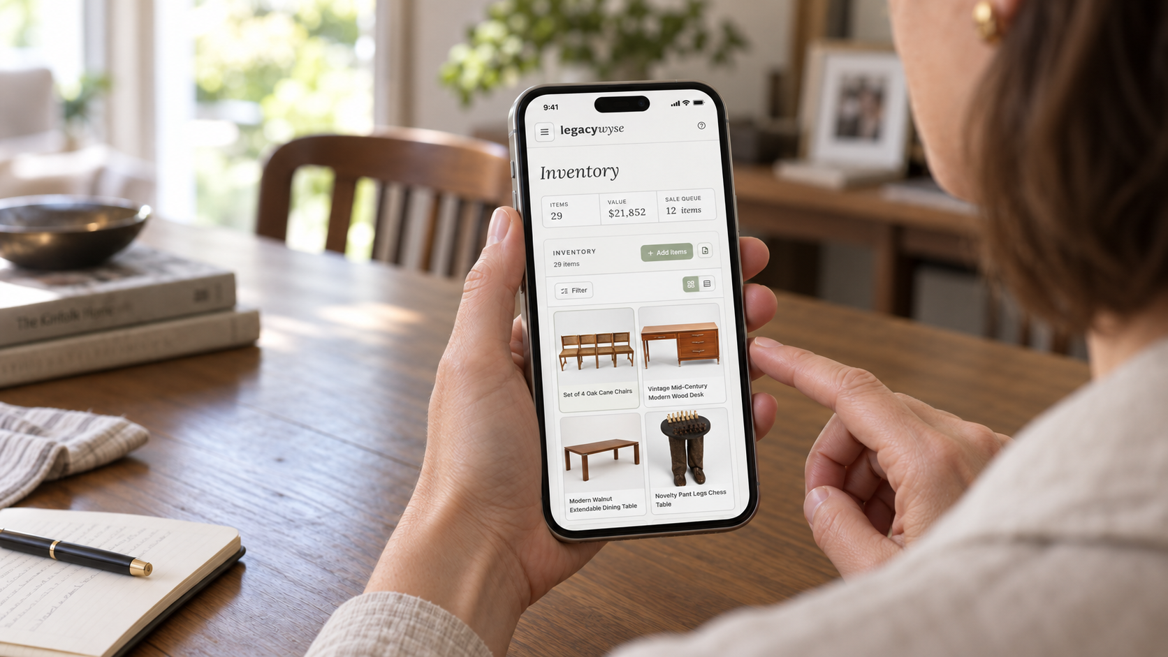 A woman using the Legacywyse Inventory page on her phone at a wooden dining table.